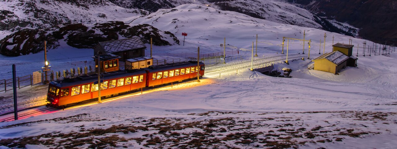 Train traveling through snow-covered Swiss Alps during winter.